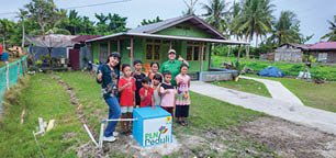 A group of people, including children, are standing in front of a house. They are posing for a picture in front of a blue cooler. AI generated content