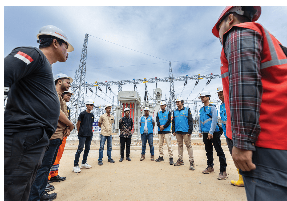 A group of construction workers wearing hard hats and safety vests are gathered around a man in a red shirt. They are standing on a dirt road and appear to be listening to the man in the red shirt. AI generated content