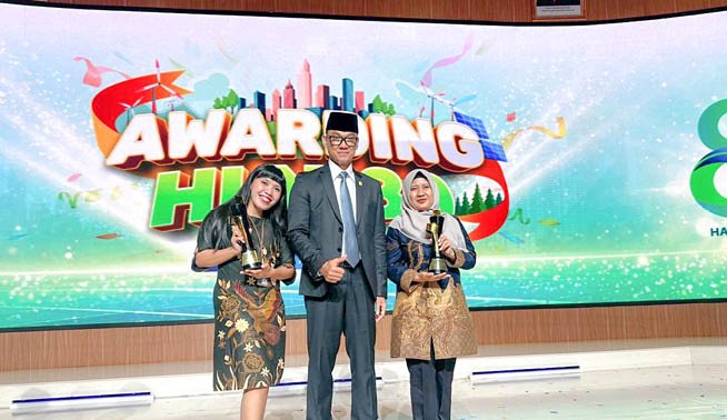 Three people are standing on a stage in front of a large screen. Two of them are holding trophies. AI generated content